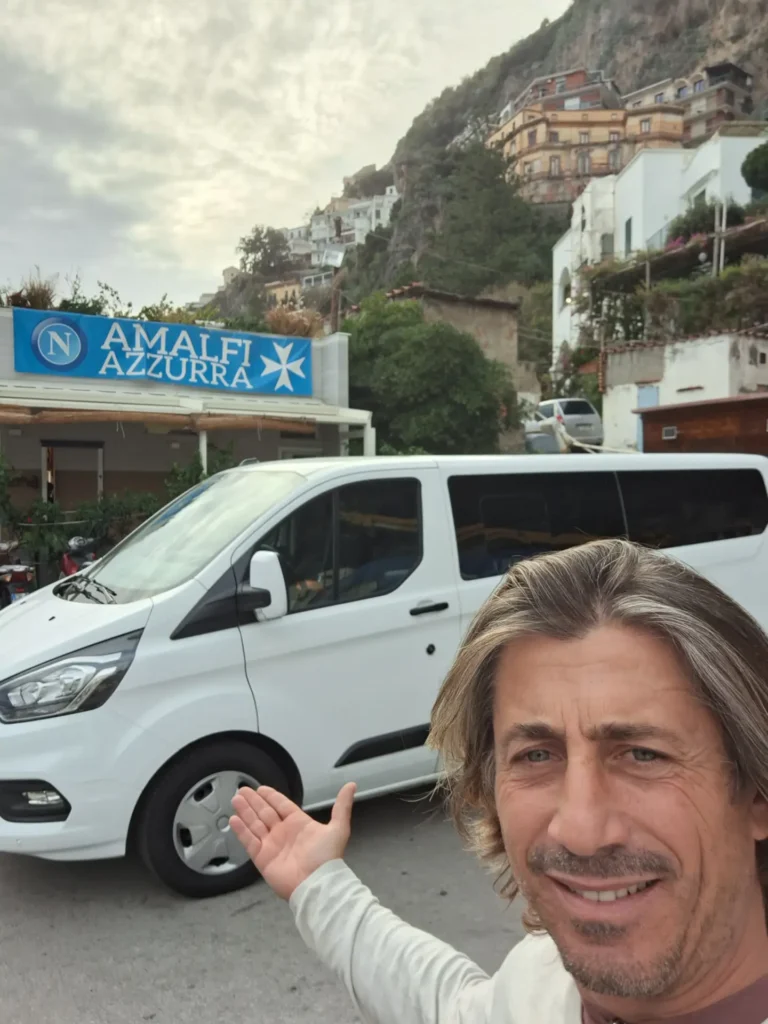 A man pointing at a white minivan with "Amalfi Azzurra" signage in the background