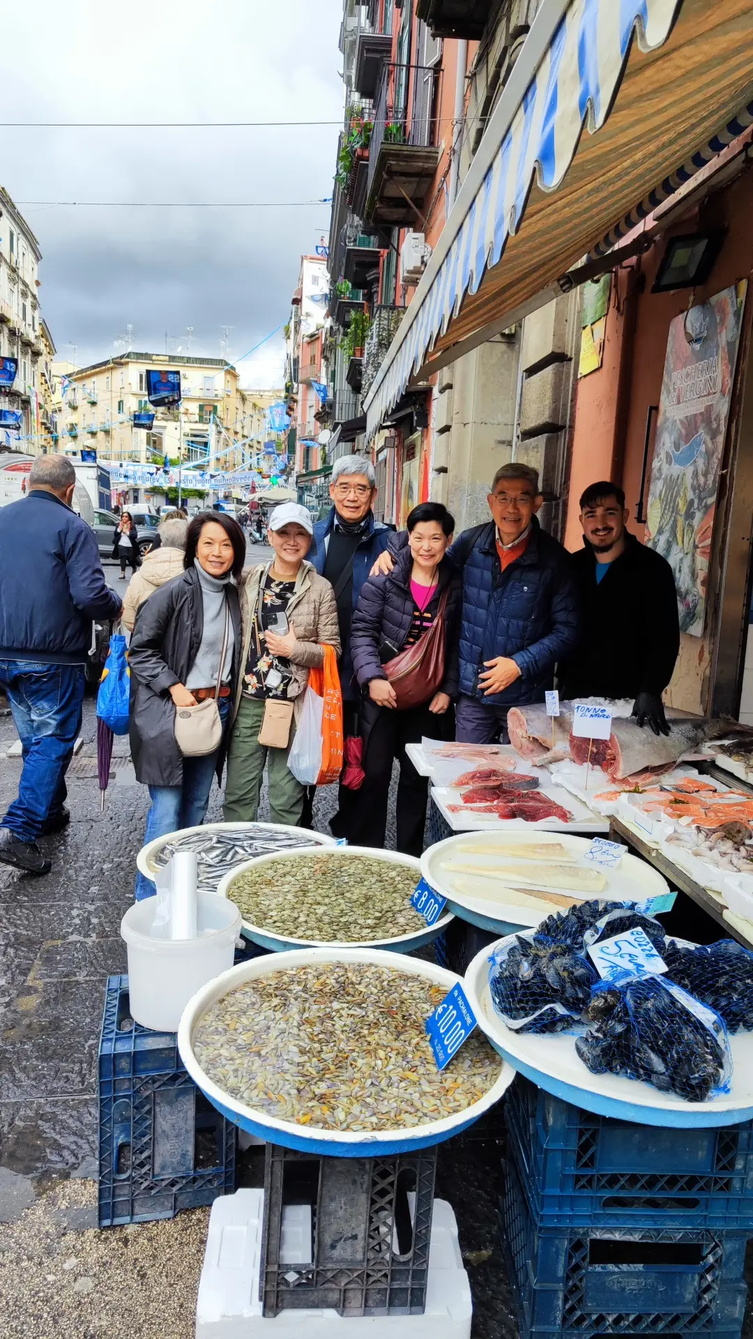 A group of tourists standing near seafood stalls in a street market in Naples