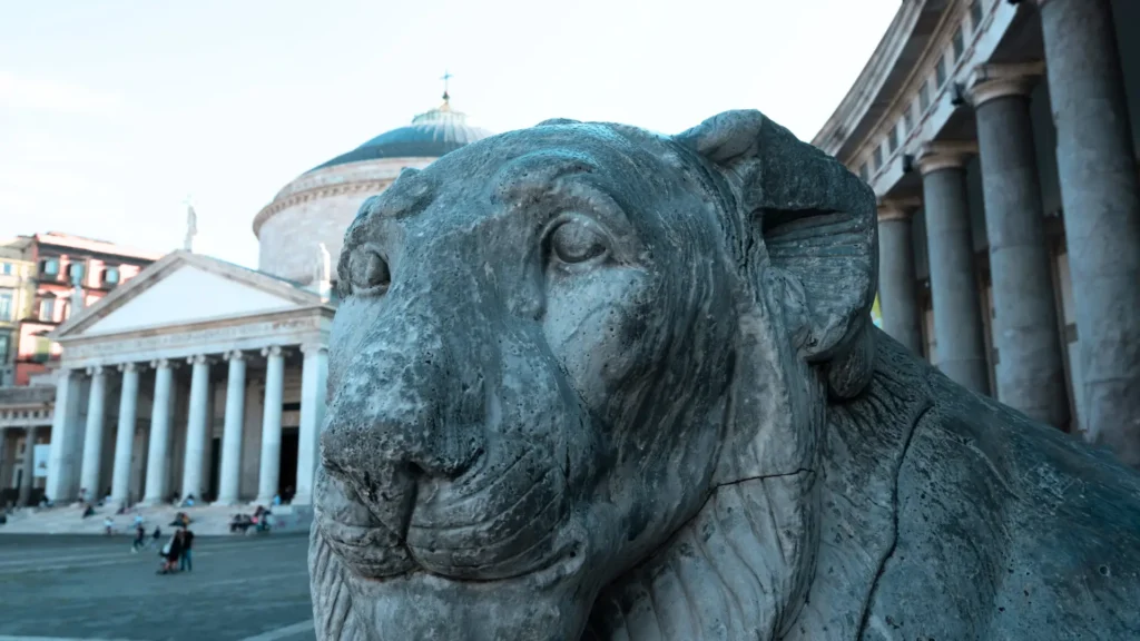 A close-up of one of the lions in Plebiscito Square, with the dome of the Royal Palace in the background